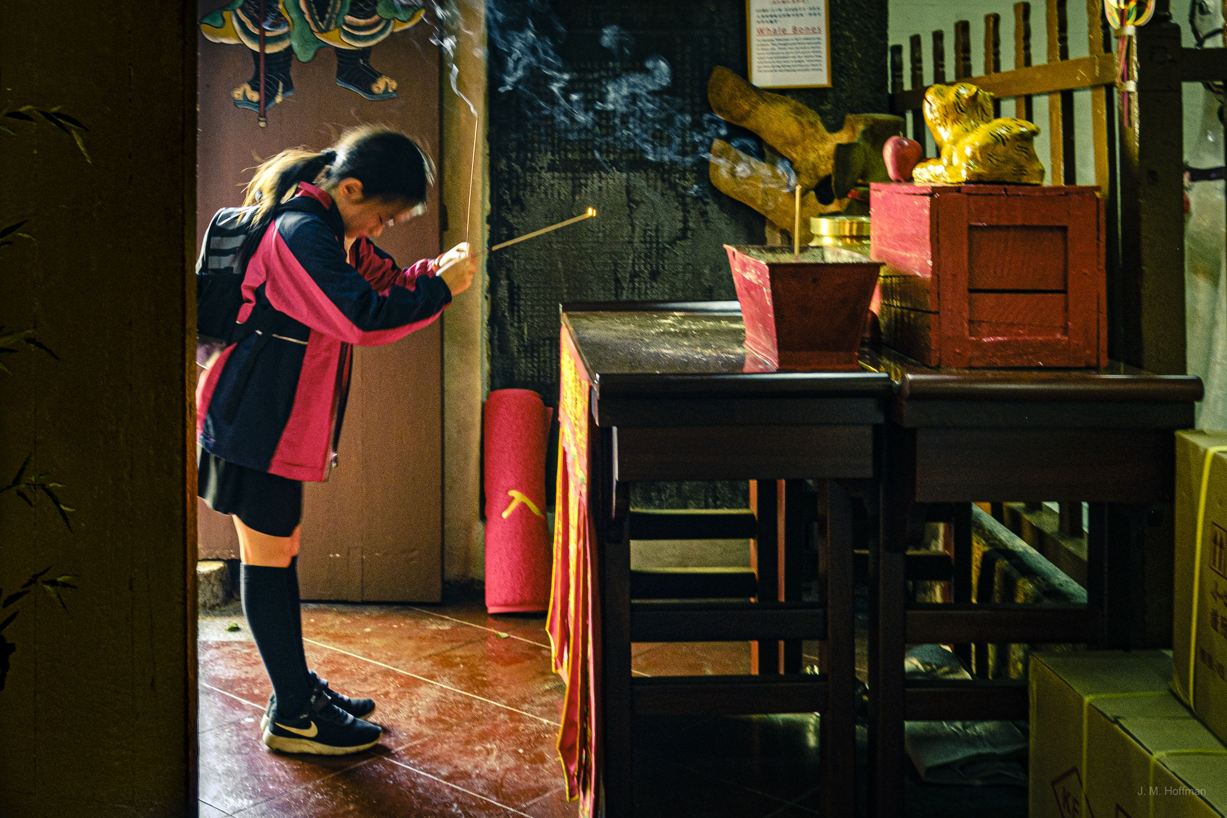A child offers incense to a local god in the Kwan Tai Temple on Tai O Island.: Tai O, Hong Kong